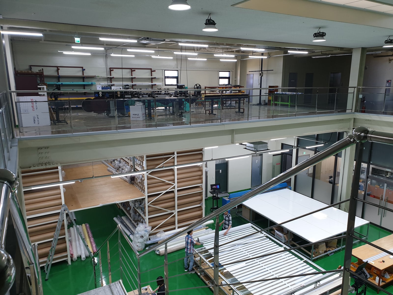 본사 공장 2층 설비와 1층 원단 보관 선반, 작업대가 보이는 모습
